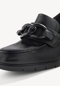 Mocassin en cuir noir avec un détail de chaîne noire épaisse sur le dessus et une semelle en caoutchouc texturée.