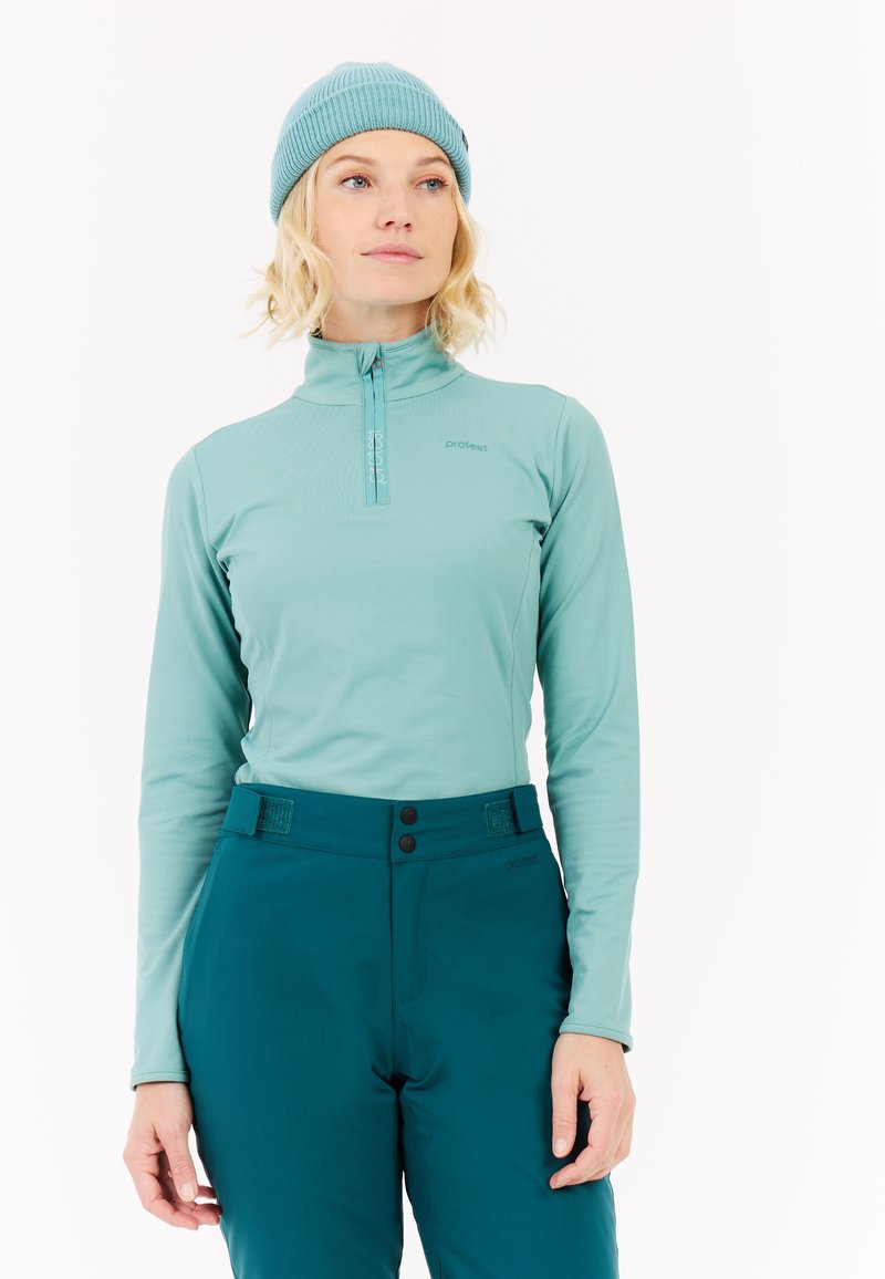 Šviesiai mėlynas ilgomis rankovėmis marškinėliai su pusiau užtrauktuku, derinami su tamsiai mėlynomis kelnėmis, kurios turi du mygtukus ir tekstūruotą juosmens dalį.