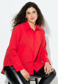 Rode knoopshirt van lichtgewicht stof, met een kraag, lange mouwen en een gerimpelde onderrand. Gecombineerd met zwarte glanzende leggings.
