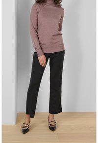 Lichtroze coltrui, gecombineerd met zwarte wijde broek en zwarte puntige hakken met bandaccenten. Glad materiaal, casual pasvorm.