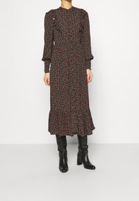Robe noire à fleurs avec de petites fleurs rouges, manches longues, ourlet volanté et corsage ajusté. Associée à des bottes noires jusqu'aux genoux.