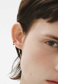 Pendiente de aro dorado con un acento azul, mostrado en una vista en primer plano de una oreja. Material suave con un acabado brillante.