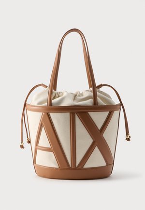 Béžová taška přes rameno z plátna s hnědým koženým lemováním, velkými písmeny "A I X", dvojitými ramenními pásky a stahovacím uzávěrem nahoře.