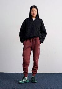 Casaco leve preto com fecho de correr, calças de jogging bordeaux e sapatilhas verdes. As características incluem punhos elásticos e bolsos laterais com fecho de correr nas calças.