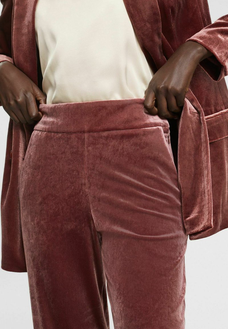 Samtige mauve Hosen mit glatter Textur und breitem Bund. Der Stoff hat einen dezenten Glanz und wird mit einem cremefarbenen Oberteil kombiniert.