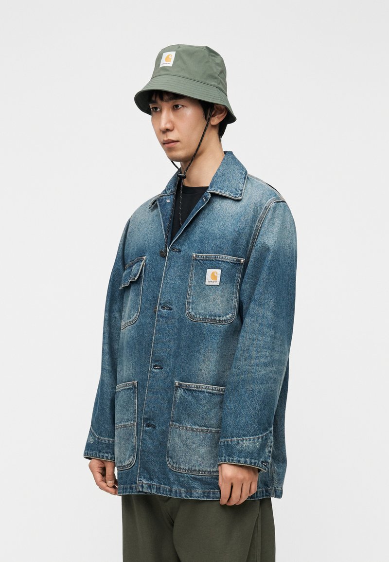 Veste en denim bleue à coupe décontractée, dotée de deux poches avant, d'une fermeture par boutons et d'un patch logo Carhartt sur la poitrine.