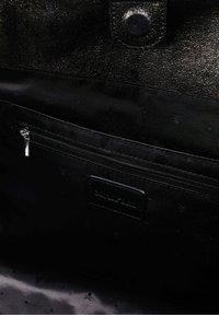 Sisätilat mustassa nahkalaukussa, jossa on sileä pinta, vetoketjullinen tasku ja kohokuvioitu logo tarrassa, kaikki tummassa kankaan vuorauksessa.