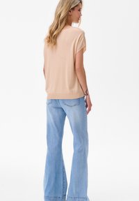 Beige gebreid topje met korte mouwen en een ronde halslijn, gecombineerd met lichtblauwe flared jeans met een vervaagde wassing en zichtbare stiksels.