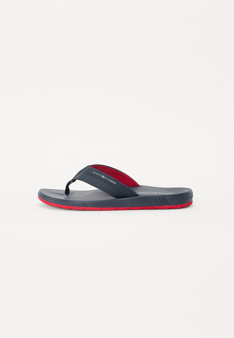 Men’s flip-flop sandal with a navy rubber strap, red accent, textured footbed, and a red sole. Features branding on the strap.