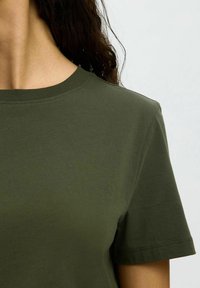 Olijf groene katoenen T-shirt met een ronde hals en korte mouwen, voorzien van een soepele textuur en minimale stikdetails.