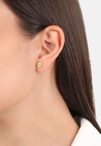 Pendientes de studs de color dorado con forma cuadrada, que presentan una piedra preciosa amarilla en el centro, rodeada de acentos transparentes.