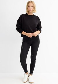 Suéter corto de punto negro con cuello redondo, combinado con jeans skinny negros con detalles desgastados y zapatillas blancas.
