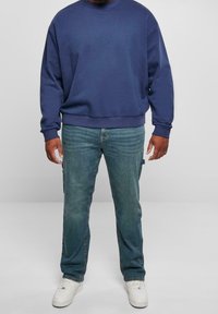 Sudadera azul marino con puños y dobladillo acanalados, combinada con jeans azules desgastados que tienen bolsillos laterales. Zapatillas blancas completan el conjunto.