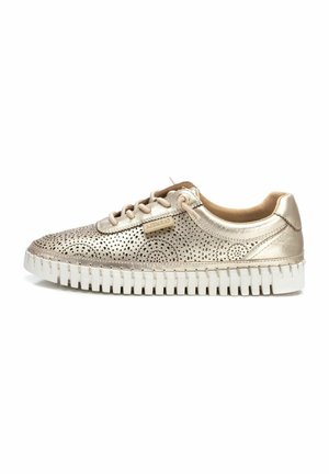 Zapatilla metálica dorada con parte superior perforada, detalles en beige y suela de goma blanca con textura estriada y cierre de cordones.