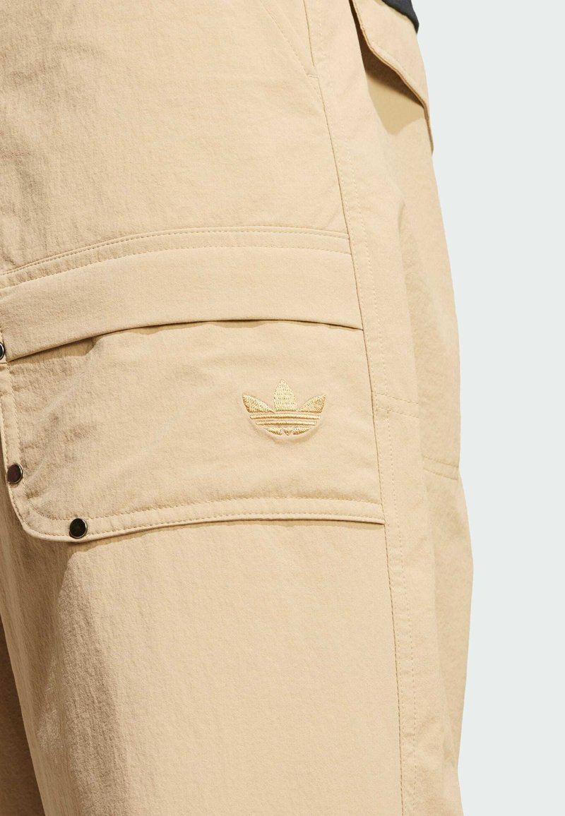 Pantaloni cargo beige realizzati in un tessuto testurizzato, con molteplici tasche e un piccolo logo ricamato sulla coscia. Accentuati da dettagli in metallo nero.