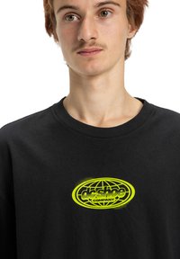 Czarny bawełniany t-shirt z okrągłym, neonowo-zielonym logo graficznym, na którym widnieje napis "dc shoe COMPANY" z kropkowymi akcentami. Krótkie rękawy, okrągły dekolt.