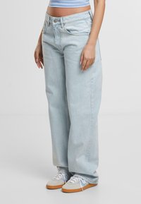 Lichtblauwe wijde spijkerbroek van denim, met een hoge taille, vijf zakken en subtiele wassing voor textuur. Gepaarde met grijze sneakers.