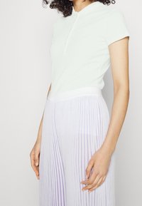 Vaalean mintunvihreä polo-paita, jossa on kaulus ja napit, yhdistettynä valkoisiin laskostettuihin housuihin, joissa on laventelivärisiä raitoja. Pehmeää kangasta ja istuva muotoilu.