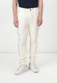 Vita ribbade sweatpants med svarta sidosträck, elastisk midja och en avslappnad passform. Värderad med vita sneakers och en marinblå topp.