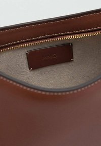 Bruine leren tas binnenkant met beige stofvoering, zichtbare gouden rits en gestikt merketiket in de binnenzak.
