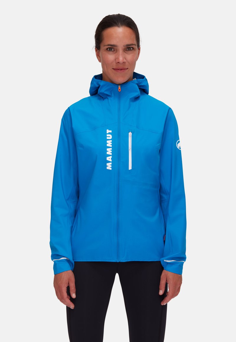 Giacca impermeabile blu con tasca sul petto con zip, cappuccio regolabile e dettagli riflettenti. Presenta un logo prominente sul davanti.