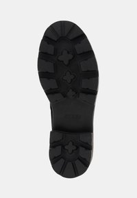 Čierna gumená podrážka so štruktúrovaným vzorom s viac smerovými drážkami a logom "GUESS".