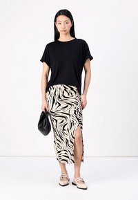 T-shirt noir à manches courtes associé à une jupe beige à imprimé zèbre avec une fente sur le côté ; le modèle tient un sac noir et porte des chaussures claires.