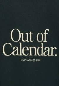 Tessuto nero con testo ricamato bianco: "Fuori dal calendario." sopra "DIVERTIMENTO IMPRONTE", con un carattere pulito e moderno.
