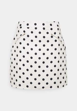 Jupe blanche avec des pois noirs, au toucher lisse. Comprend deux poches latérales zippées et un ourlet droit.