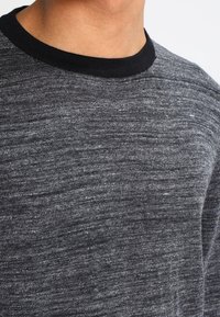 Grå texturerad sweatshirt med en svart ribbad halsringning. Tyget har ett melerat mönster som ger djup åt utseendet.