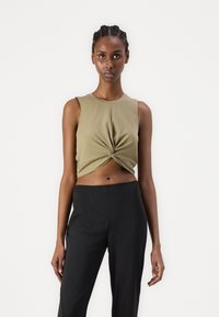 Olive green cropped sleeveless top with a twisted front detail, paired with black high-waisted pants, featuring a smooth fabric texture.