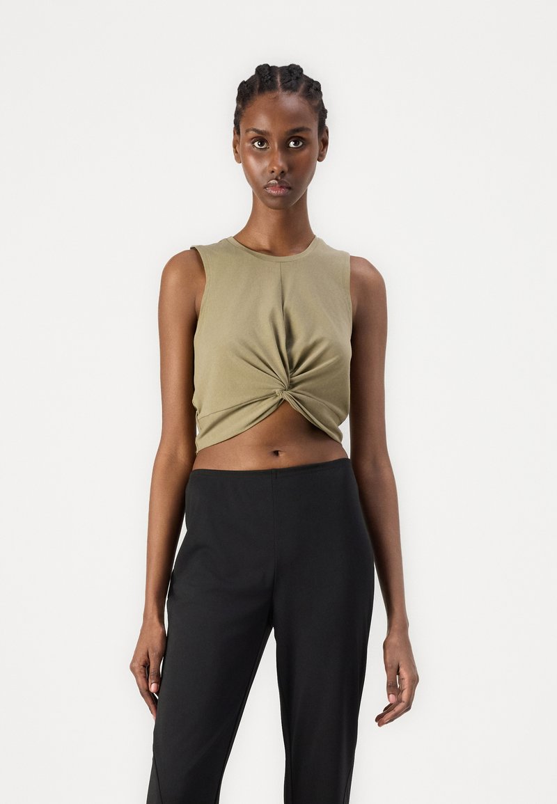 Olive green cropped sleeveless top with a twisted front detail, paired with black high-waisted pants, featuring a smooth fabric texture.