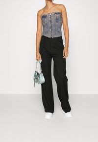 Denim strapless korselett med dragkedja framtill, ihopparad med svarta vida byxor och vita slipskor. Håller en liten iridescerande väska.