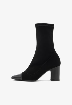 Black ankle boot made of a soft textile with a smooth leather toe cap. Features a block heel and a fitted sock-like design.