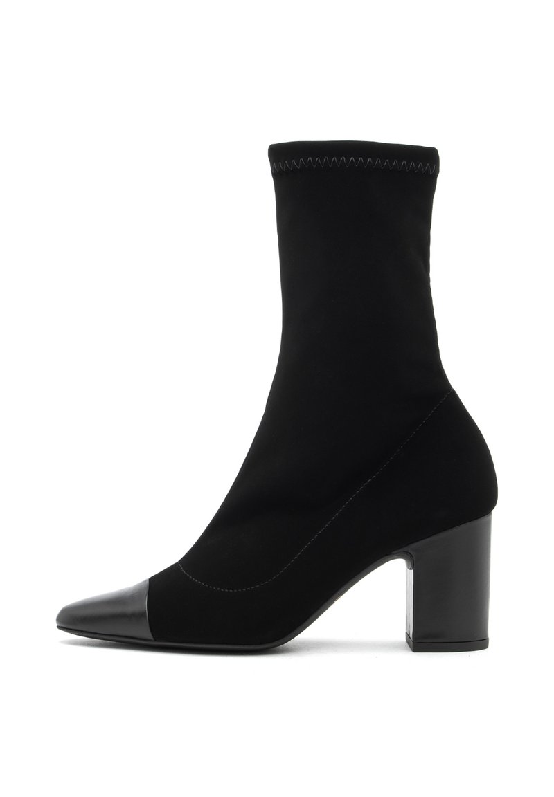 Bota negra hasta el tobillo hecha de un textil suave con una puntera de cuero liso. Presenta un tacón cuadrado y un diseño ceñido similar a un calcetín.