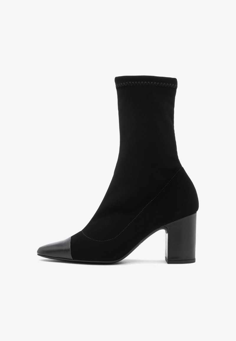 Bota negra hasta el tobillo hecha de un textil suave con una puntera de cuero liso. Presenta un tacón cuadrado y un diseño ceñido similar a un calcetín.