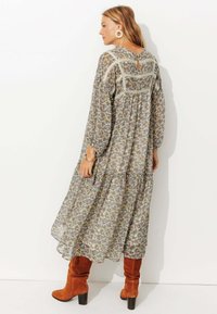 Robe midi à fleurs avec des manches longues, dotée d'un dos en trou de serrure, d'une taille froncée et d'une jupe à volants. Portée avec des bottes en suede marron jusqu'au genou.