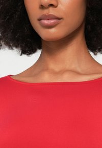 Piros, testhez simuló felső széles, egyenes nyakkal és sima textúrával; a váll és a kulcscsont területe hangsúlyos.