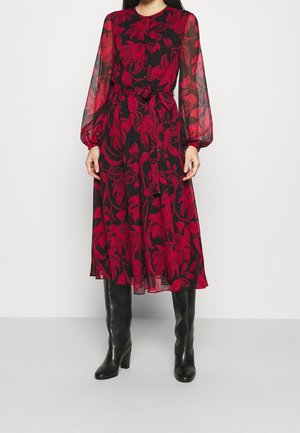 Zwarte midi-jurk met rood bloemmotief, doorschijnende lange mouwen, taille-strikceintuur, gecombineerd met zwarte kniehoge laarzen met hak.