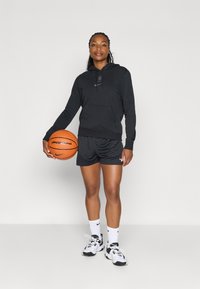 Svart hettegensere med logo, sorte mesh-shorts og hvite sportssko. Holder en oransje basketball med teksten "playground".