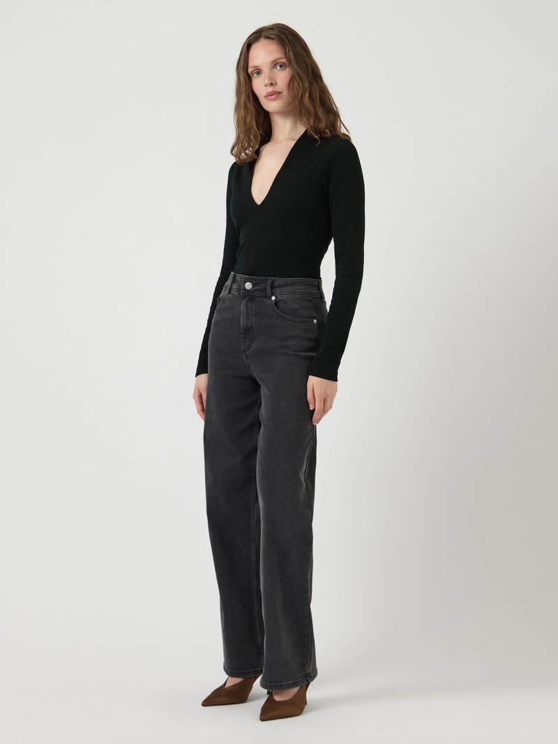 Svart ribbestrikket langermet bodysuit med dyp V-hals, kombinert med høytlivs mørkegrå vide jeans og brune spisse hæler.
