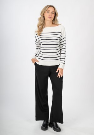 Weißer Pullover mit marineblauen Streifen, lockere Passform, weites Ausschnitt; kombiniert mit schwarzen weit geschnittenen Hosen und klobigen schwarzen Stiefeln.