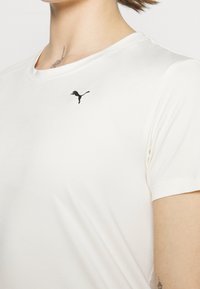 Bílý tričko vyrobené z měkké látky s kulatým výstřihem a krátkými rukávy, s malým černým logem Puma na hrudi.