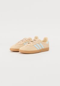 Beige sneakers med en tekstureret overdel, lyseblå tre striber og gummisål. Designet med en rund tå og snørelukning.
