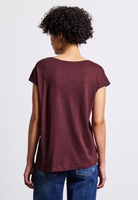 Haut court à manches courtes bordeaux avec une coupe décontractée et un col rond, associé à un jean en denim bleu, montrant une texture lisse.