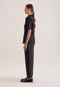 Czarna koszula z krótkim rękawem i ciemne spodnie noszone z czarnymi loafersami. Koszula ma kołnierzyk i prosty krój oraz gładką fakturę.