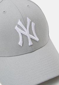 Grå baseball cap lavet af stof, med et hvidt broderet New York-logo. Struktureret form med en buet skygge og tekstureret overflade.