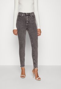 Vysoké skinny džíny v bledě černé džínovině. Mají pět knoflíků, přední kapsy a minimální švy. V kombinaci s nahými sandály na podpatku.