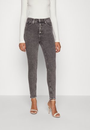Jeans ajustados de cintura alta en denim negro desgastado. Cuenta con cinco botones, bolsillos delanteros y costuras mínimas. Combinados con tacones nude con tiras.