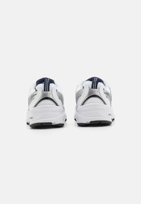 Chaussures de sport blanches avec des accents argentés, des panneaux en maille et des détails bleu marine au talon, présentant une semelle texturée et un design de soutien.